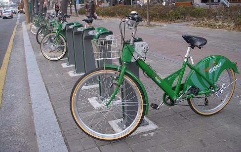 Image is of bikes in a row.  They're parked along the sidewalk.
