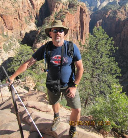 Photo is of Doug hiking in Utah.  He stands for a photo with what looks like a white cane in his hand.